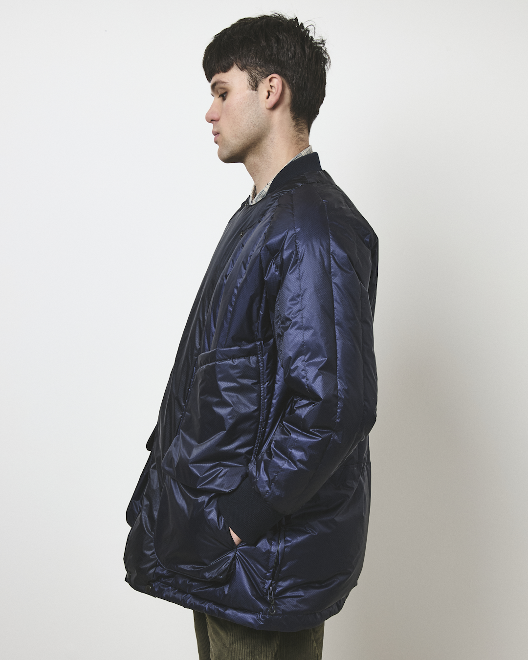 Profile view of a man in a navy blue quilted puffer jacket layered over a checkered shirt.