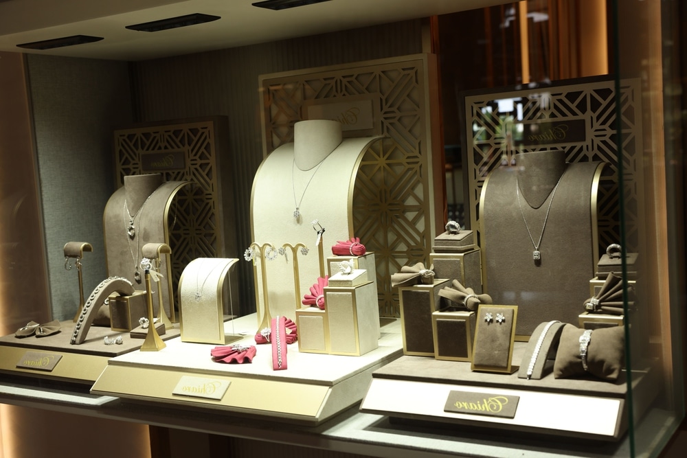 A luxury jewelry display case with elegant gold and beige tones showcasing coordinated sets of necklaces and earrings.