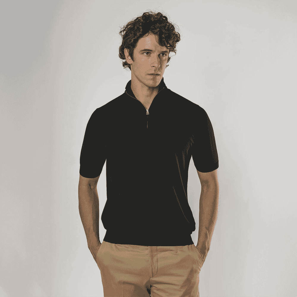 Man in a black short-sleeve quarter-zip knit sweater and beige trousers.