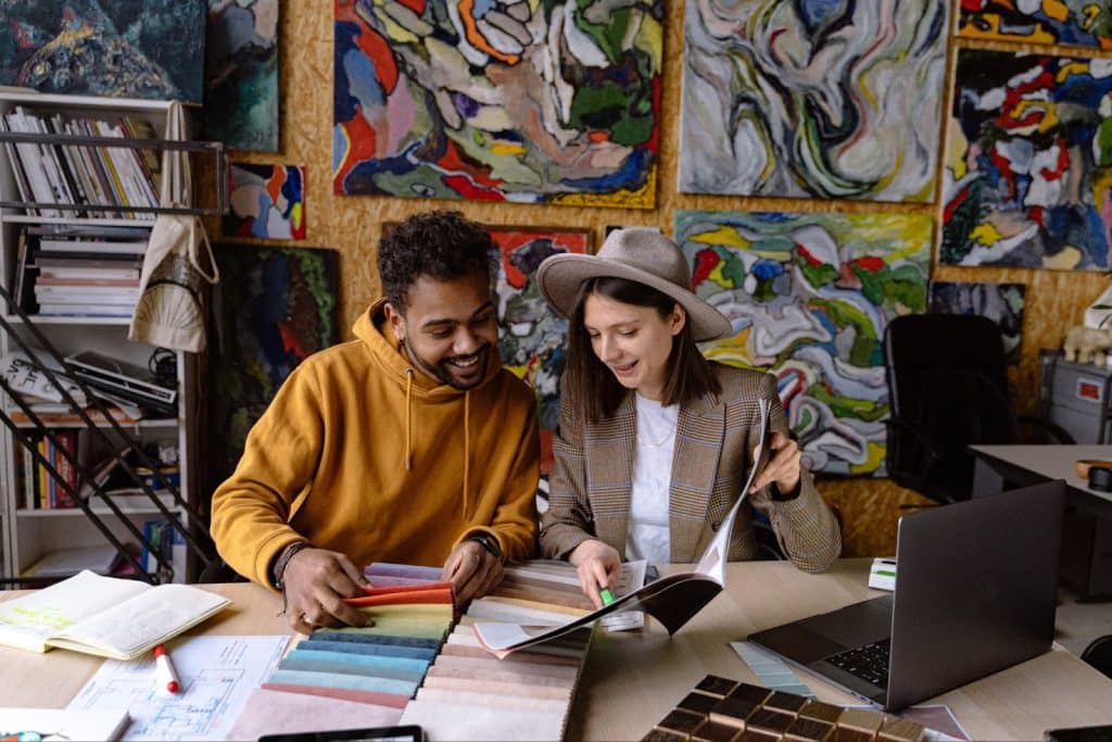 A man and woman in a creative studio reviewing fabric swatches and design materials at a desk.
