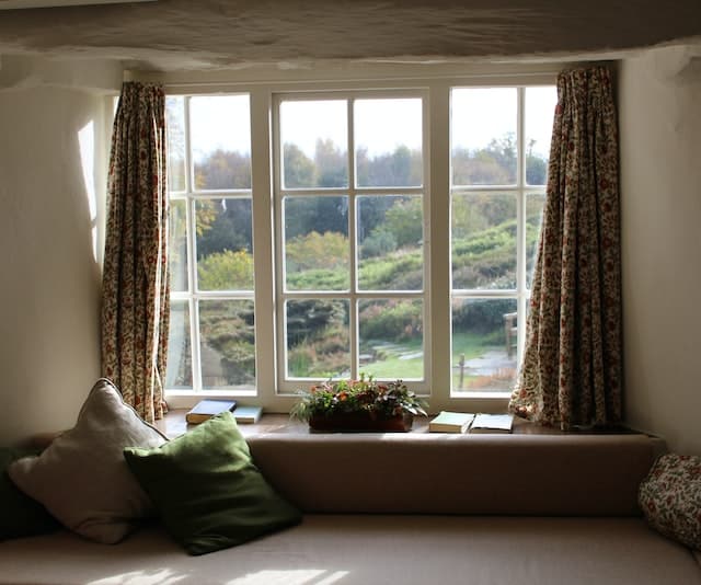 Cozy window seat with floral curtains and green cushions overlooking a garden.