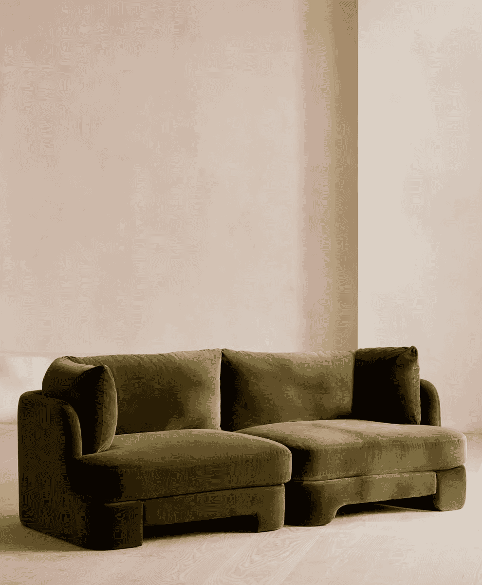 Olive-green velvet modular sofa in a minimalist room with light wood floors.