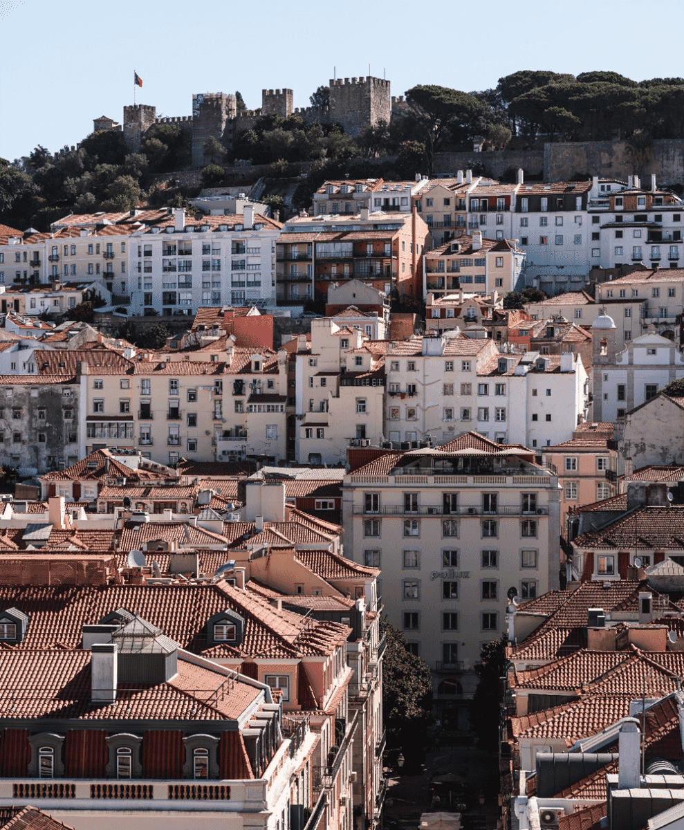 Panoramic sunset view of Lisbon's terracotta roofs and a historic castle on the hill.