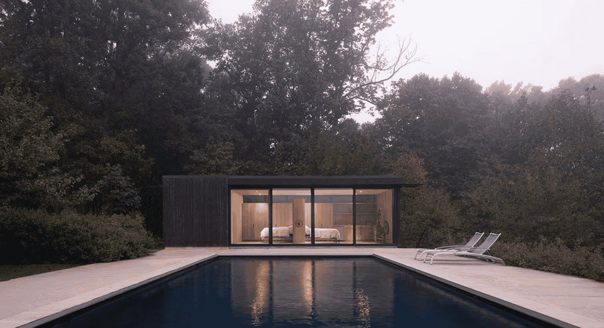 Outdoor swimming pool adjacent to a modern glass-walled pavilion surrounded by dense green forest.