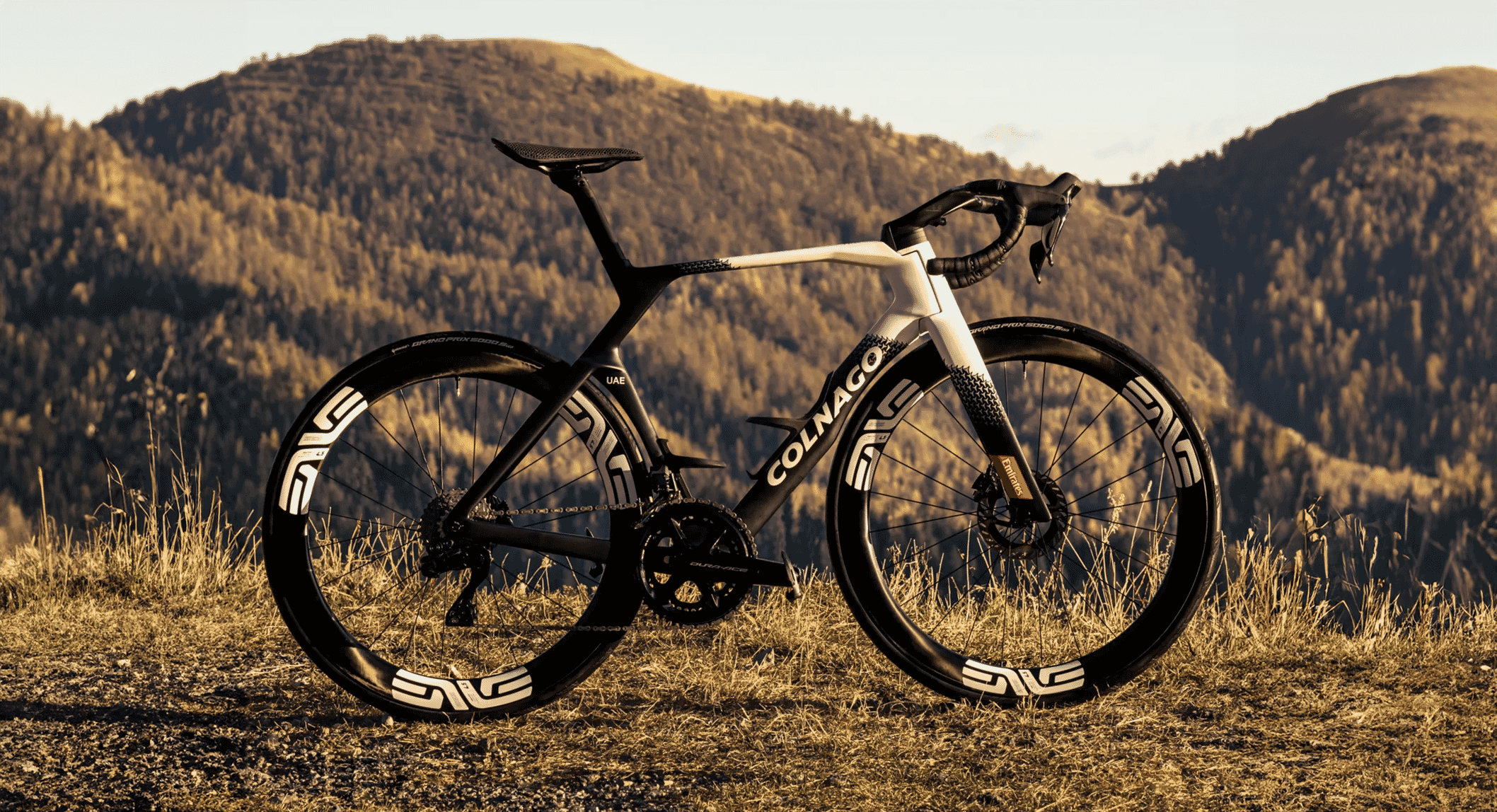 A sleek Colnago road bicycle with black and white frame and ENVE wheels on a sunlit mountain hillside.