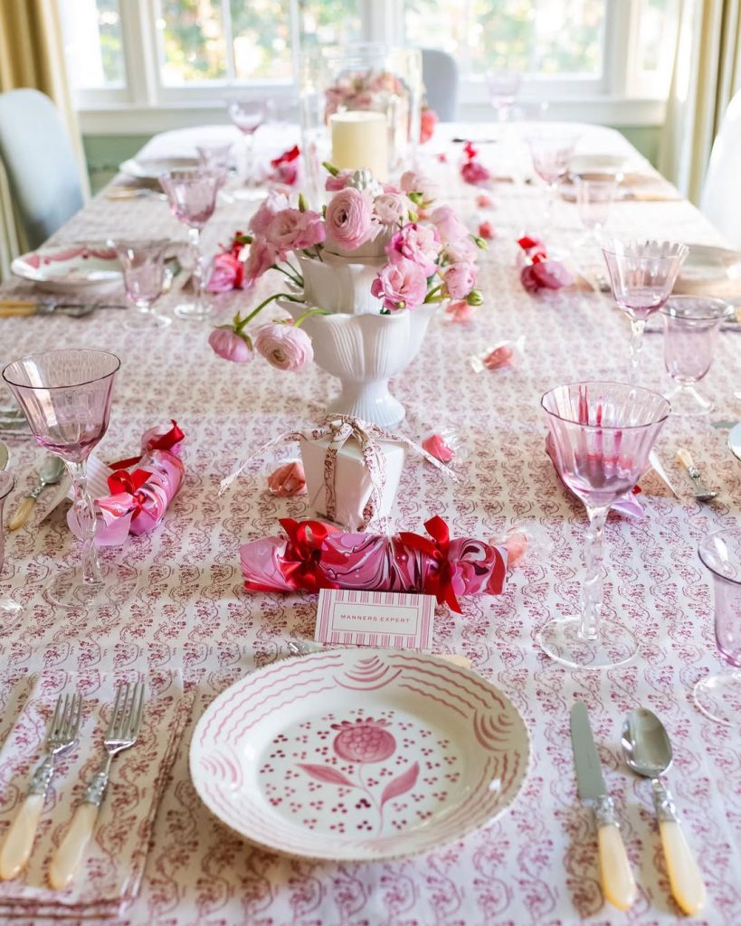 An elegant dining table set with pink flowers, vintage-style glassware, and patterned linens.