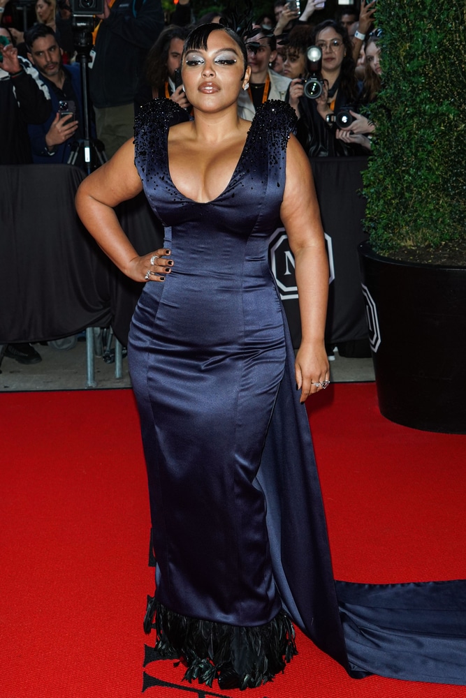 Paloma Elsesser in a navy blue satin plunging gown with a feathered hem on a red carpet.