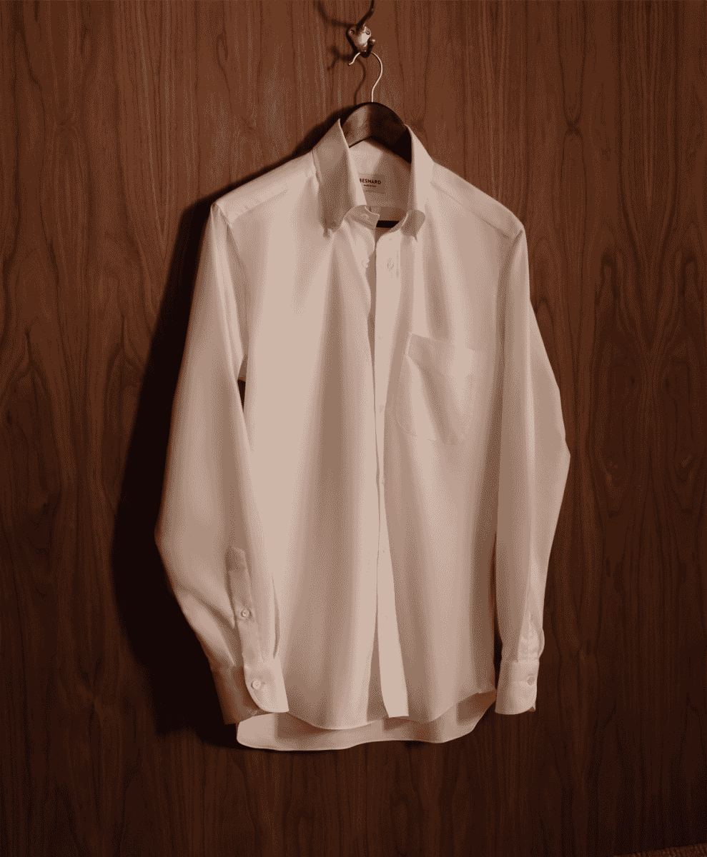 A crisp white dress shirt on a wooden hanger against a dark wood-paneled wall.