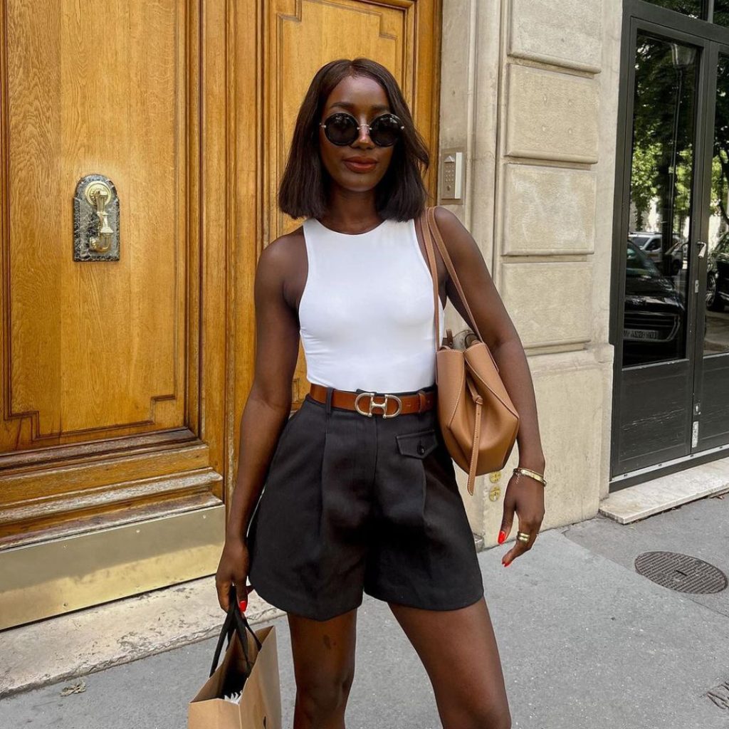 Aida Badji wearing a white tank top with tailored shorts and a belt.