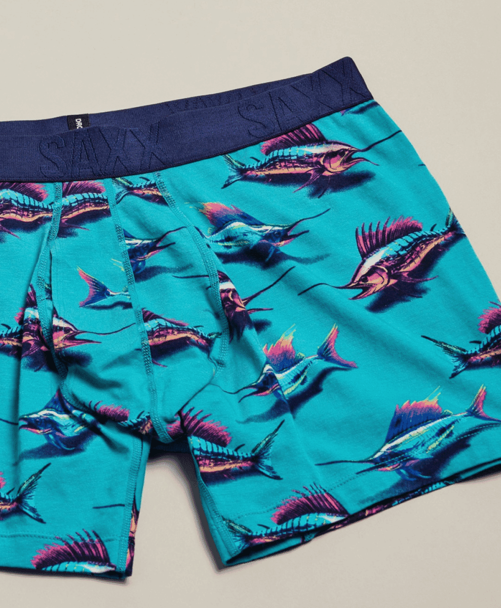 Teal SAXX boxer briefs with a vibrant marlin fish pattern and branded navy waistband.