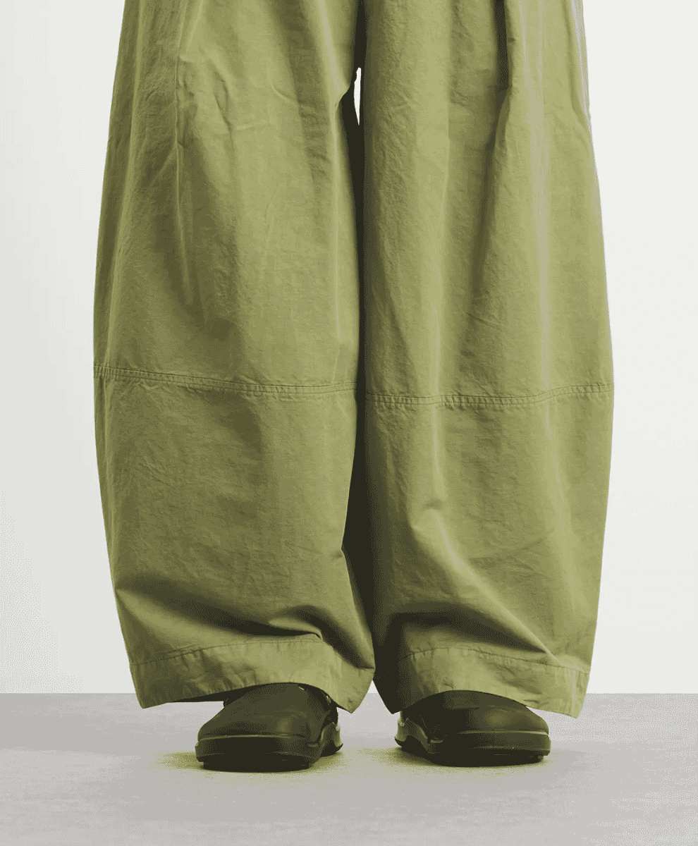 Close-up of a person wearing wide-leg olive-green trousers and black commando-sole slip-on shoes.