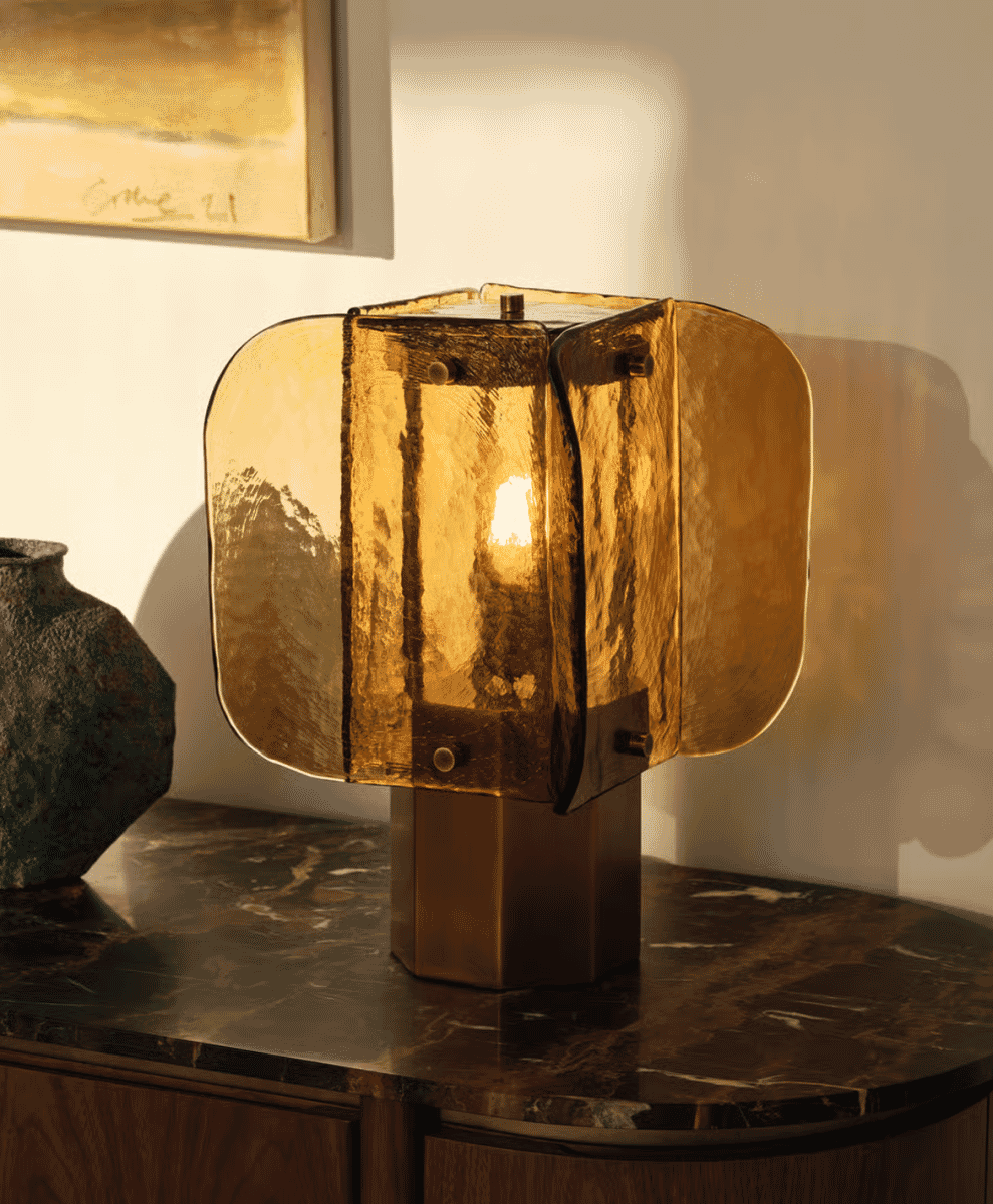 Golden textured table lamp casting a warm glow on a dark marble console table.