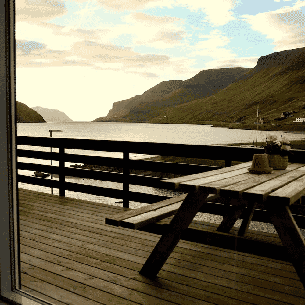 Wooden deck with a picnic table overlooking a serene fjord and green mountains.