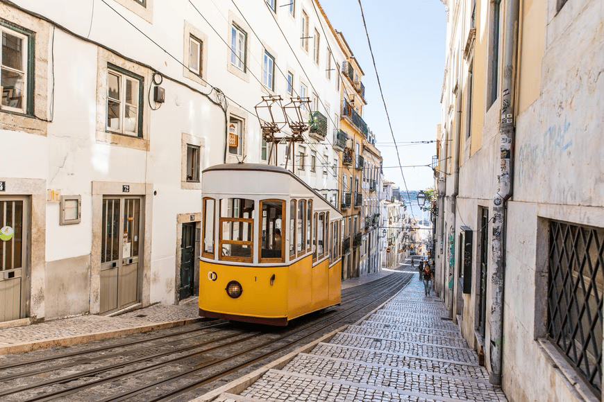 A yellow vintage tram on a steep Lisbon street with a pedestrian in the background.