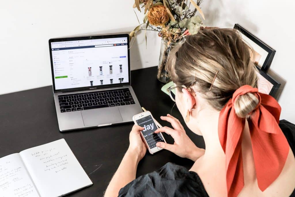 A woman with a red scarf in her hair working with a smartphone and laptop at a desk.