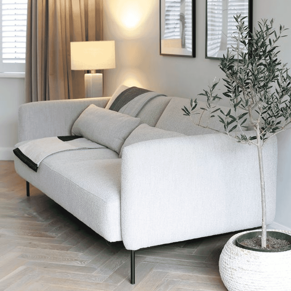 White bouclé sofa with cushions on a herringbone floor alongside an olive tree.