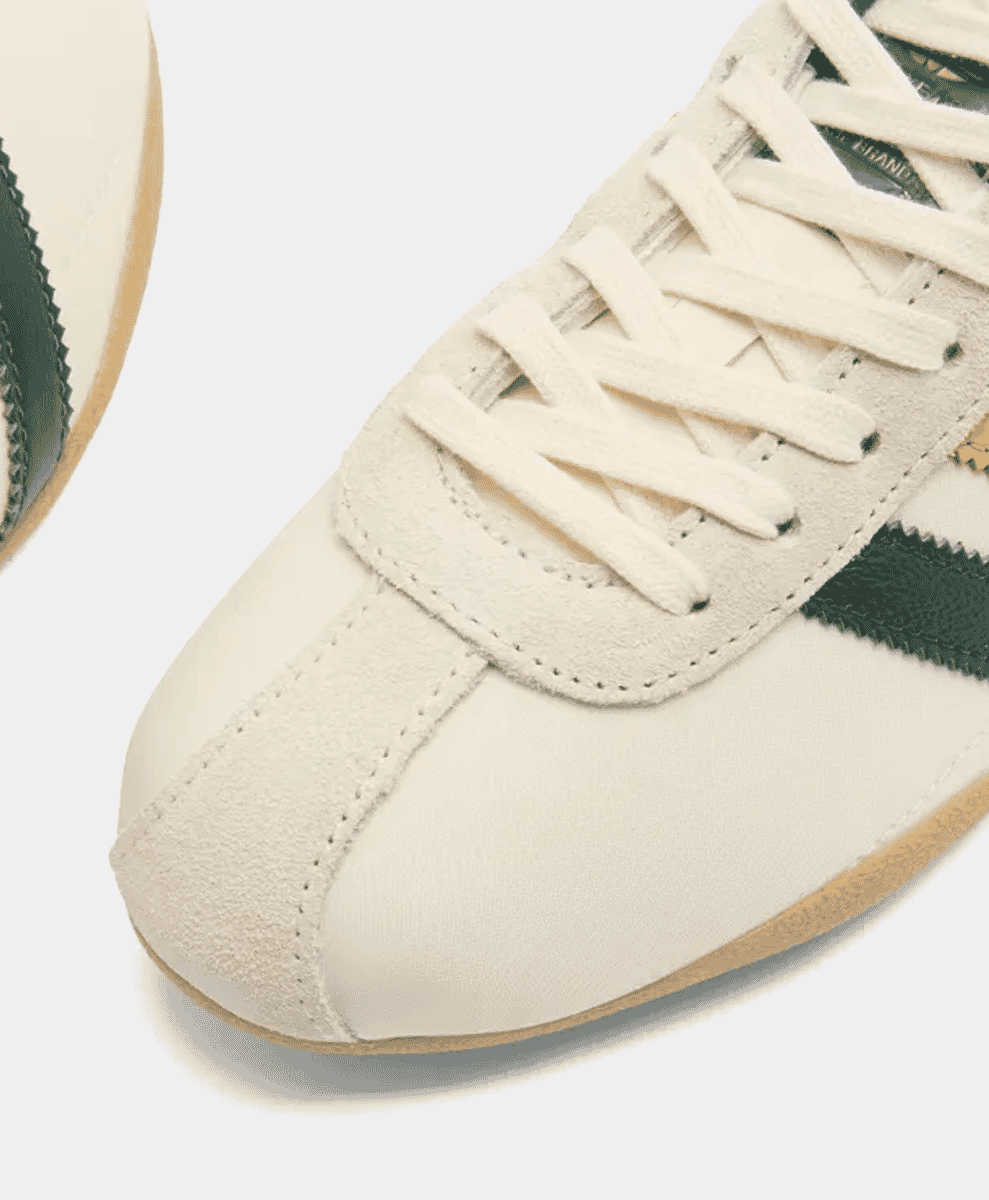 Close-up of Collegiate Green stripes and gum sole on a cream Adidas sneaker.
