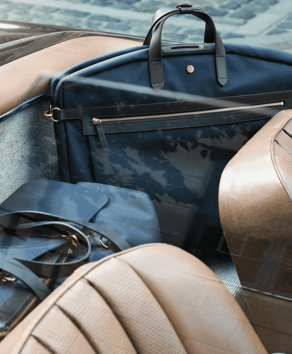 A navy blue leather-trimmed travel bag and accessories inside a luxury car with beige leather seats.