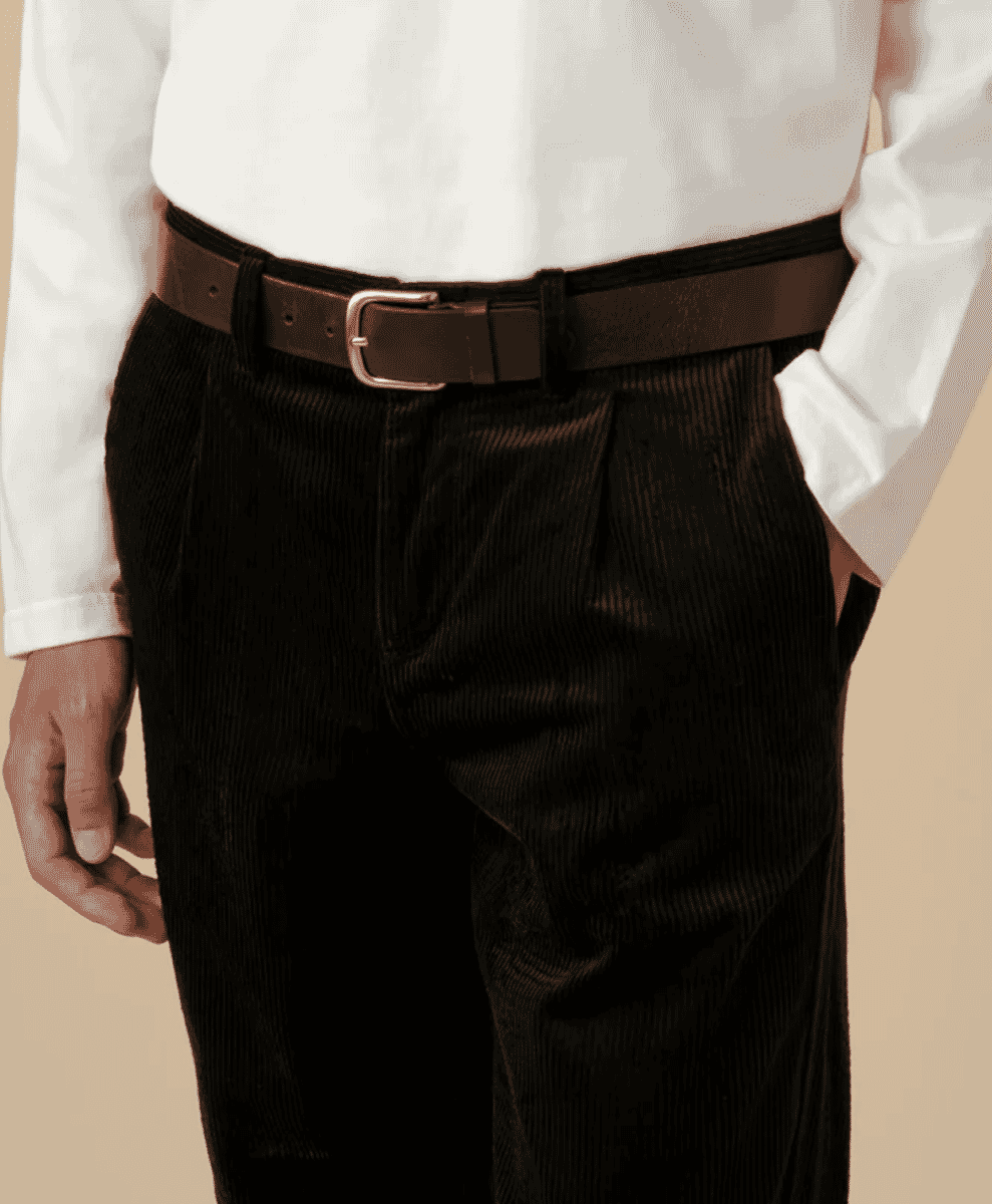 Close-up of dark corduroy pleated trousers with a brown leather belt.