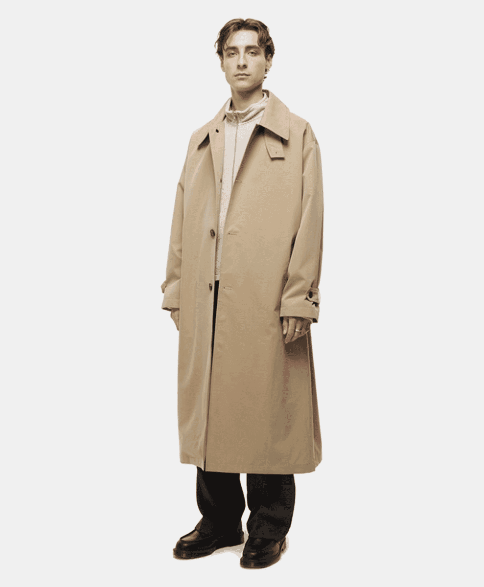 Model wearing a long beige mfpen trench coat with a relaxed fit over a smart-casual outfit.