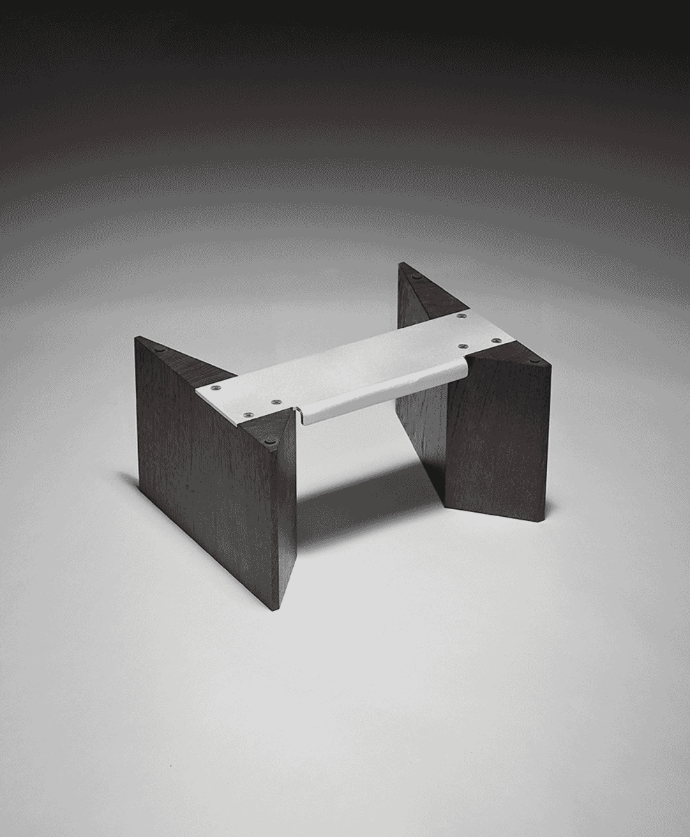A modern minimalist bench with dark wooden legs and a metallic seat in a studio environment.