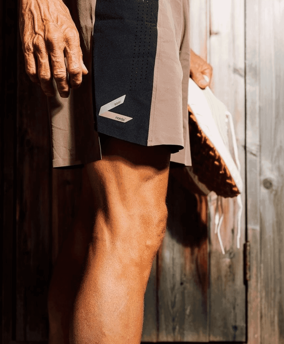 Close-up of a runner wearing Soar Norda technical shorts against a rustic wooden backdrop.