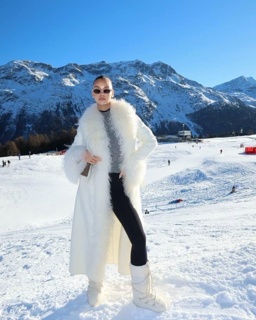 Woman in a white fur coat and black leggings in a mountain landscape.