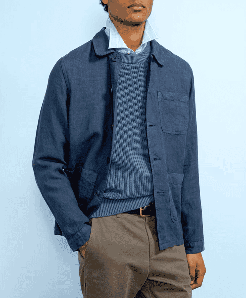 Man layering a navy blue linen overshirt over a knit sweater and light trousers.