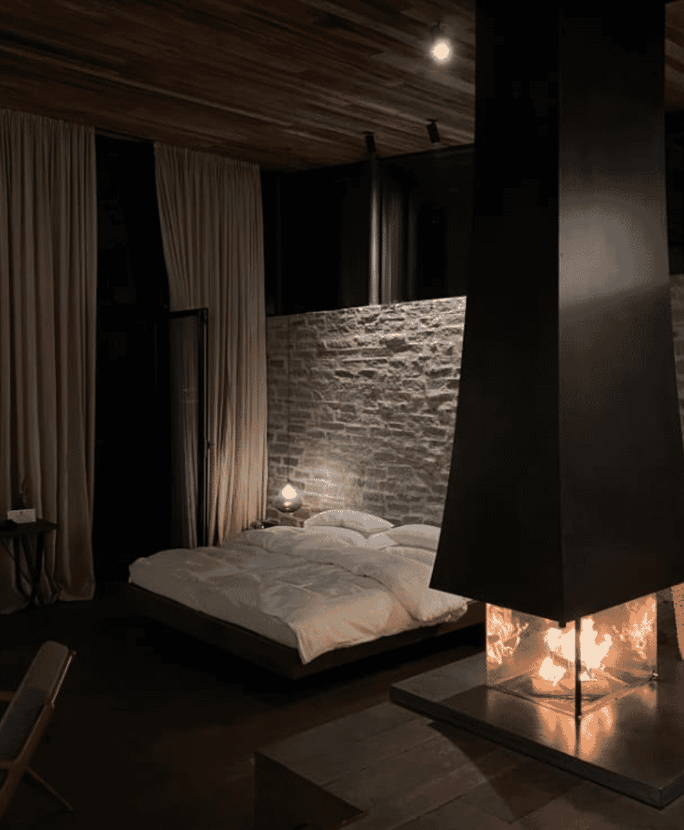 Modern bedroom interior with a black fireplace hood set against a stone wall.