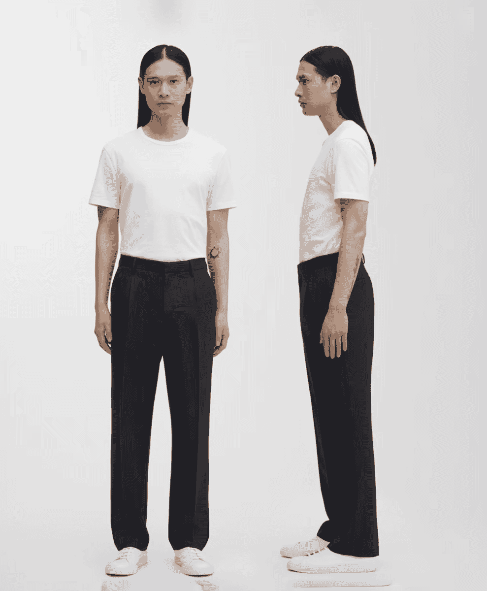 Full-body studio shot of a man wearing pleated wool trousers and white sneakers.