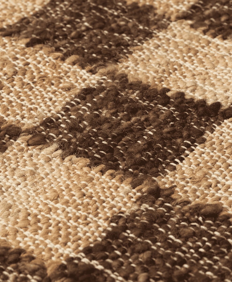 A close-up of a textured jute rug with earthy brown and beige checkered patterns.
