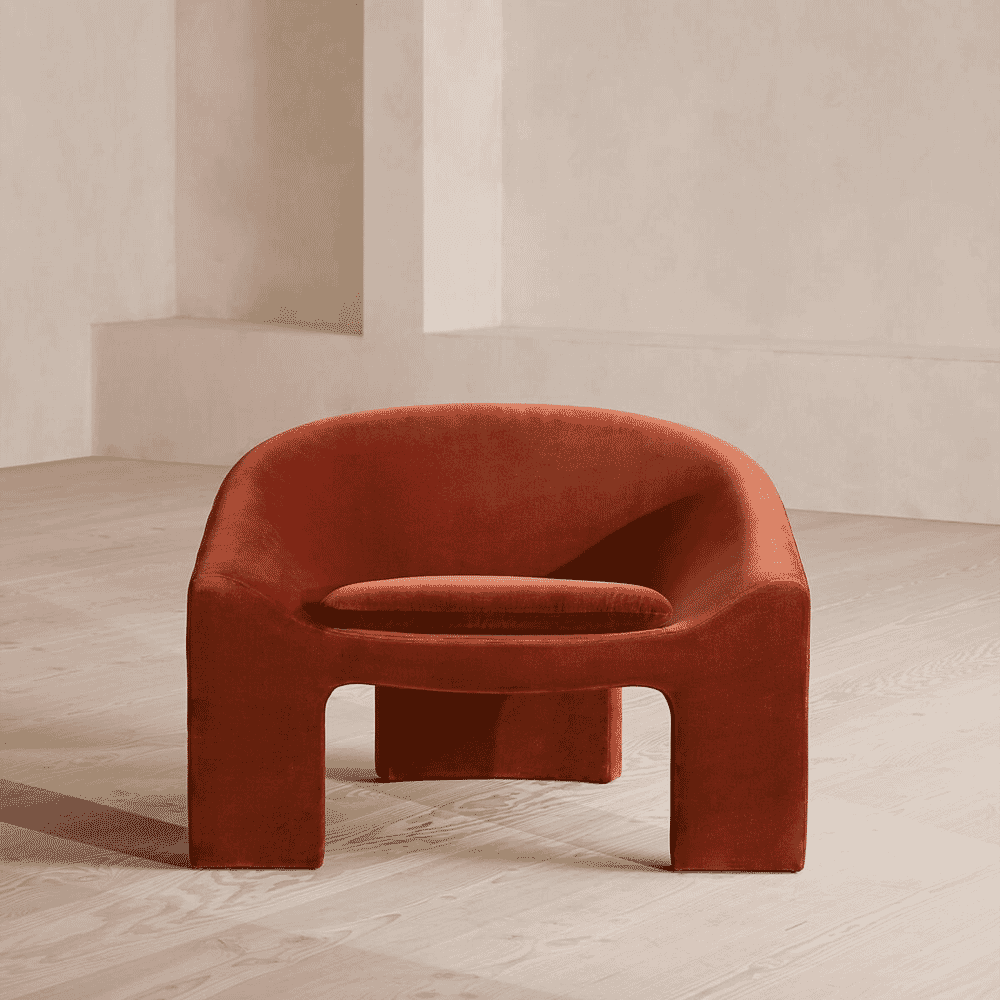 A terracotta velvet armchair with sculptural block legs on a light wood floor.