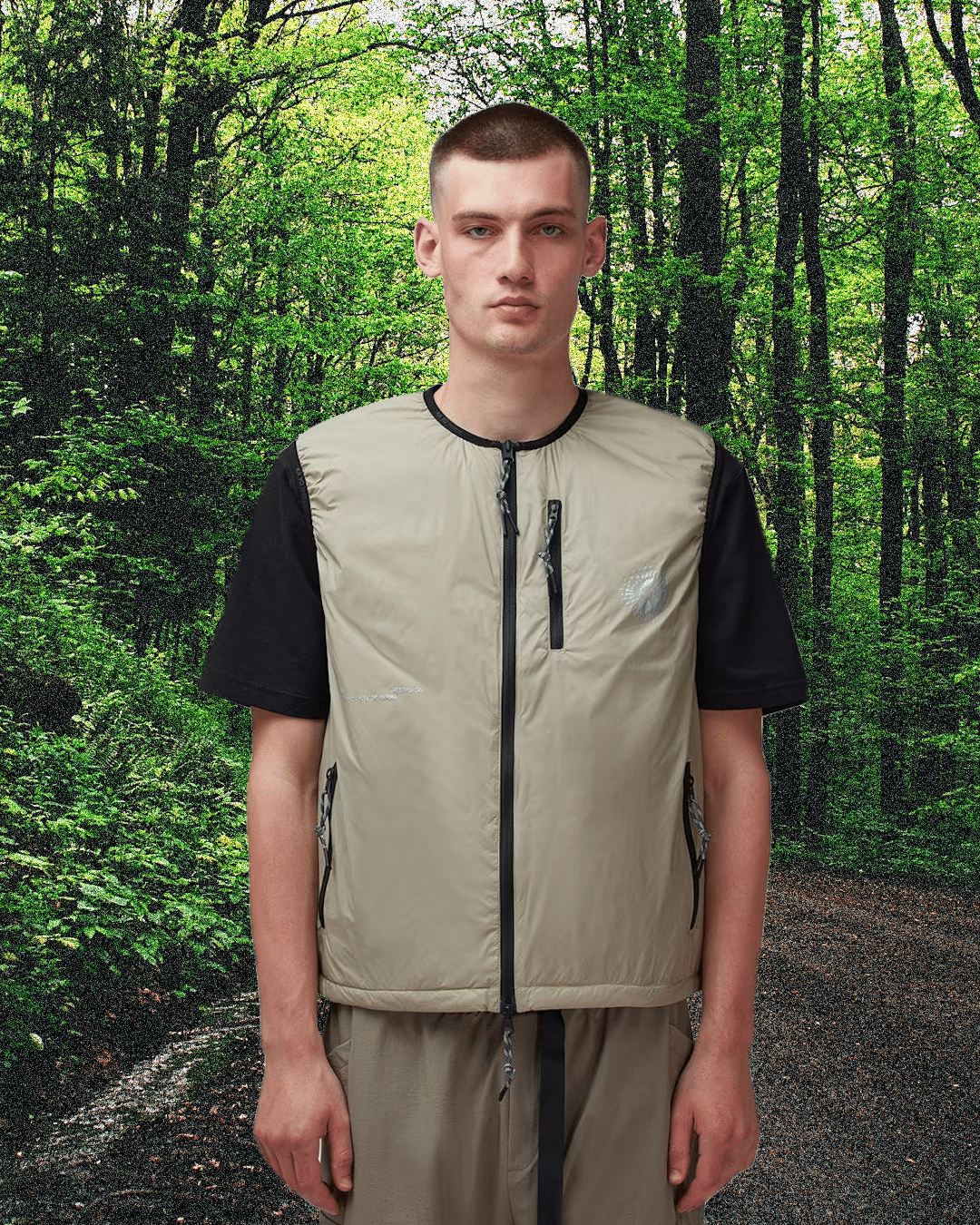 A model in a beige quilted vest and matching pants in a forest setting.