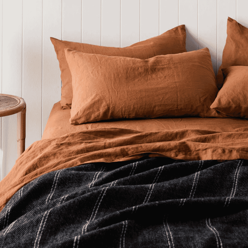 Terracotta linen bedding layered with a dark striped throw blanket against a white wall.