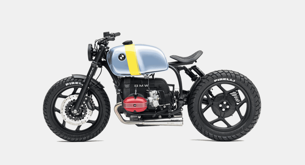 Side profile of a custom BMW cafe racer with a light blue fuel tank and red engine accents in a white studio.