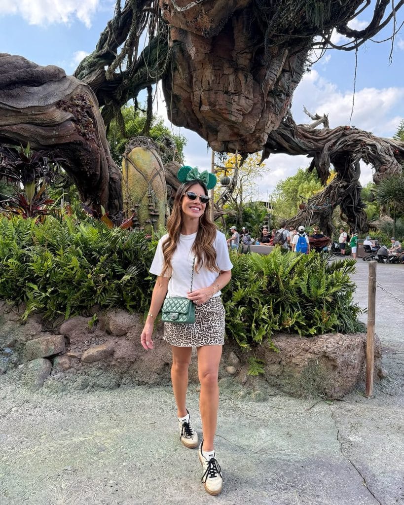 A woman in a white t-shirt and leopard-print skirt wearing chunky sneakers and green Minnie Mouse ears.