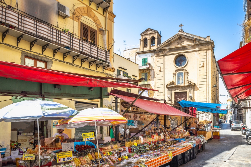 Busy outdoor street market with people in casual fashion near a historic church.