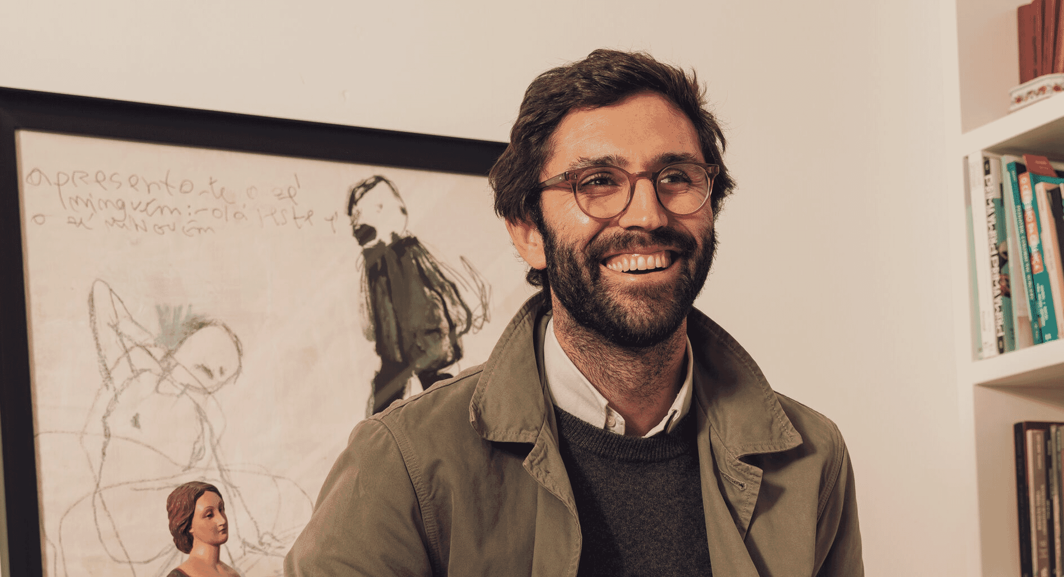 Bearded man in an olive jacket and white shirt posing in a stylish indoor room