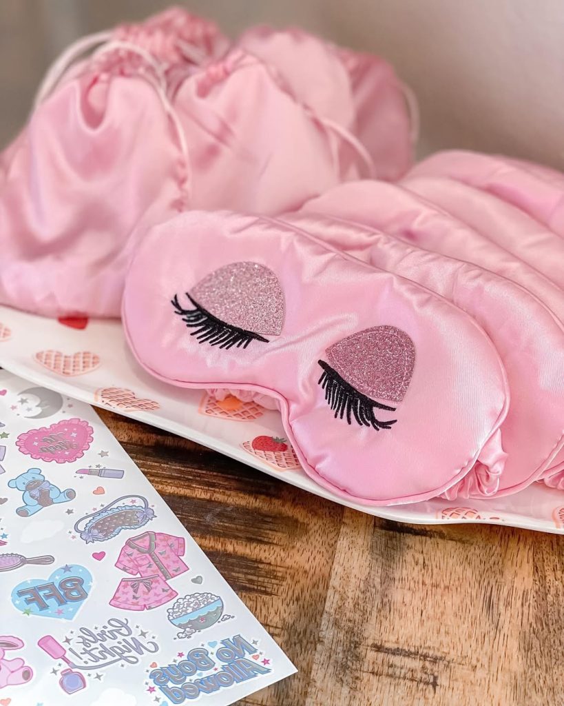 Pink satin sleep masks with glittery eyelash embroidery on a decorative tray.