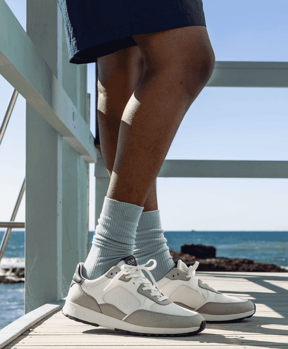 A person on a wooden pier overlooking the ocean wearing CLAE sneakers and blue ribbed socks.
