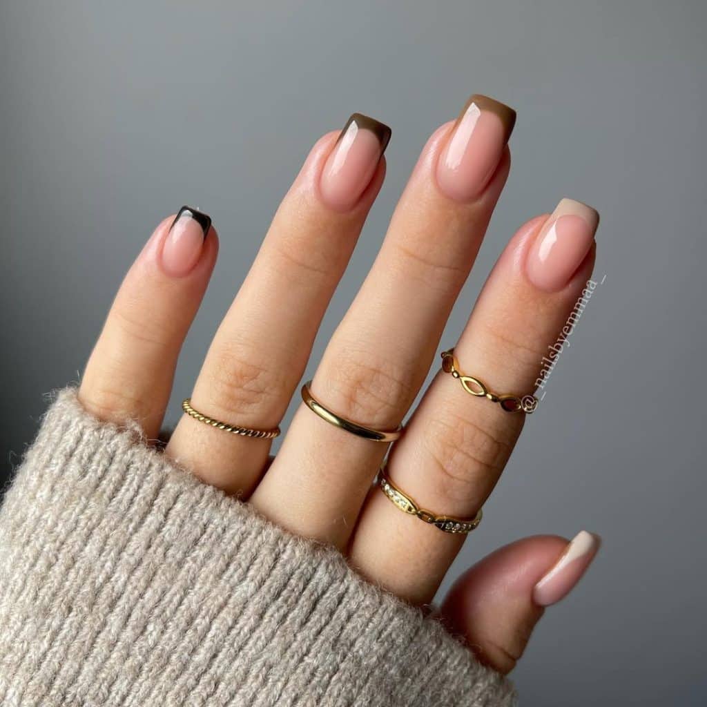 Nude and brown-tipped nails with multiple gold rings and a beige sweater.