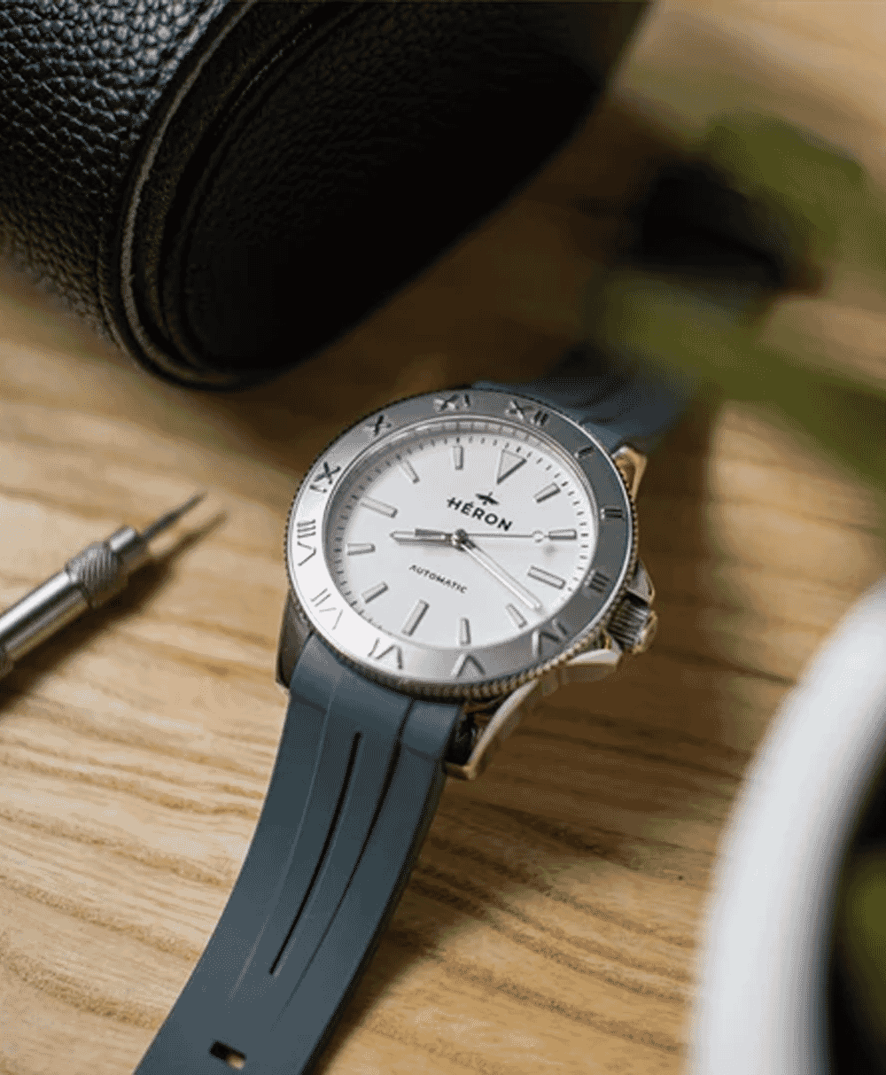 A Heron automatic wristwatch with a white dial and blue rubber strap on a wooden surface.