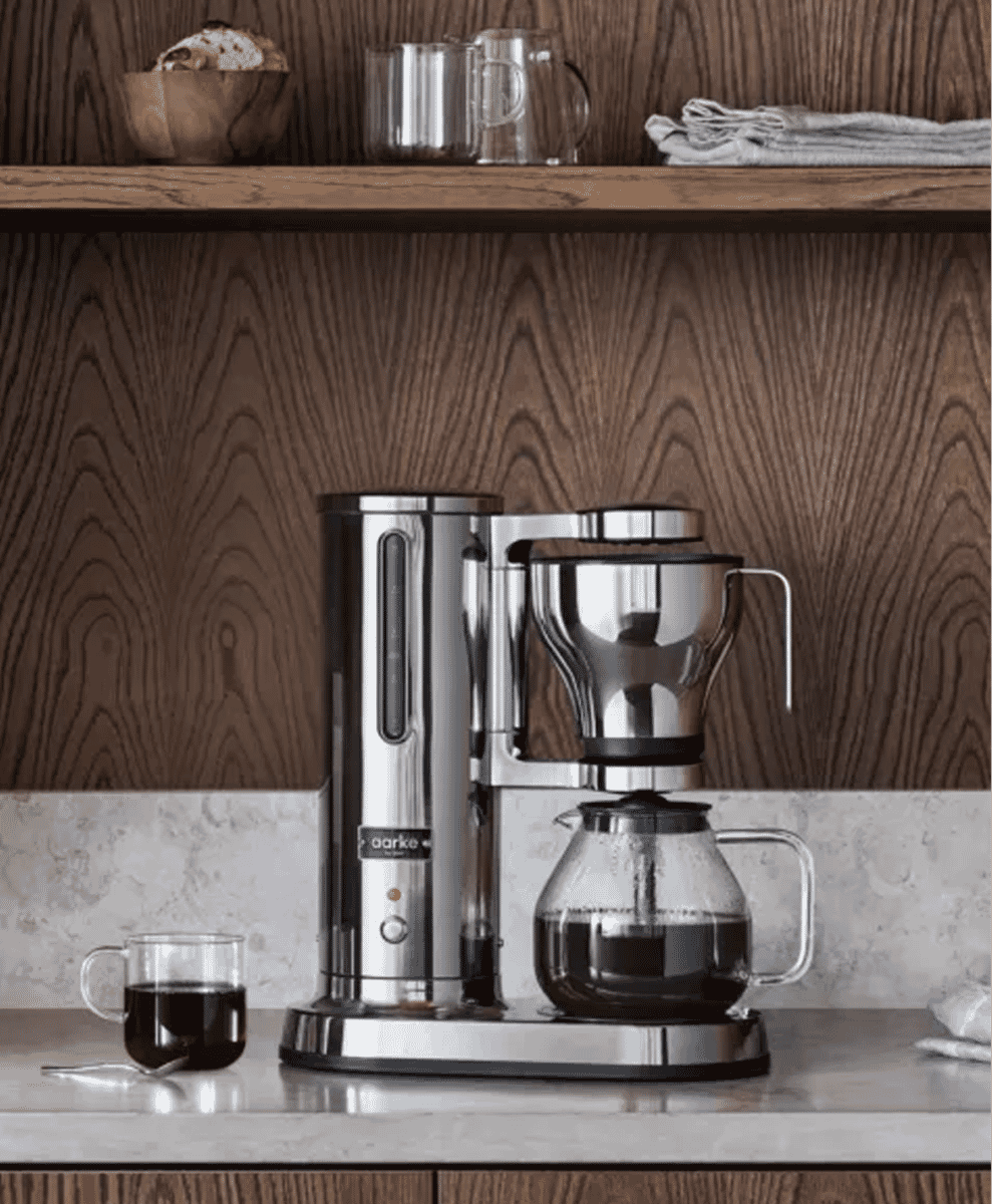 A stainless steel Aarke drip coffee maker on a marble kitchen countertop.