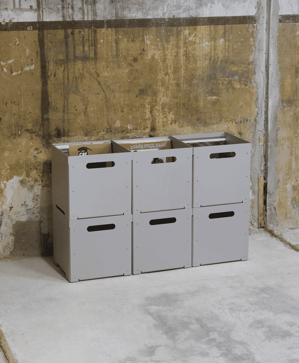 Three gray modular storage bins arranged against a weathered concrete wall.