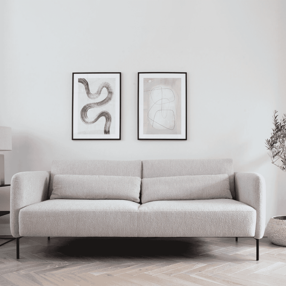 A beige textured modular sofa in front of a white wall decorated with two minimalist abstract art prints.
