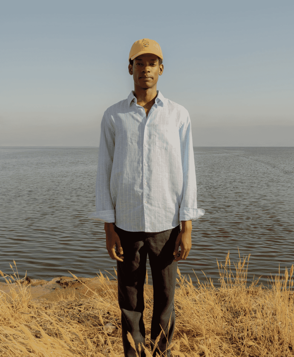 Man wearing mustard yellow cap and blue striped shirt by the water.