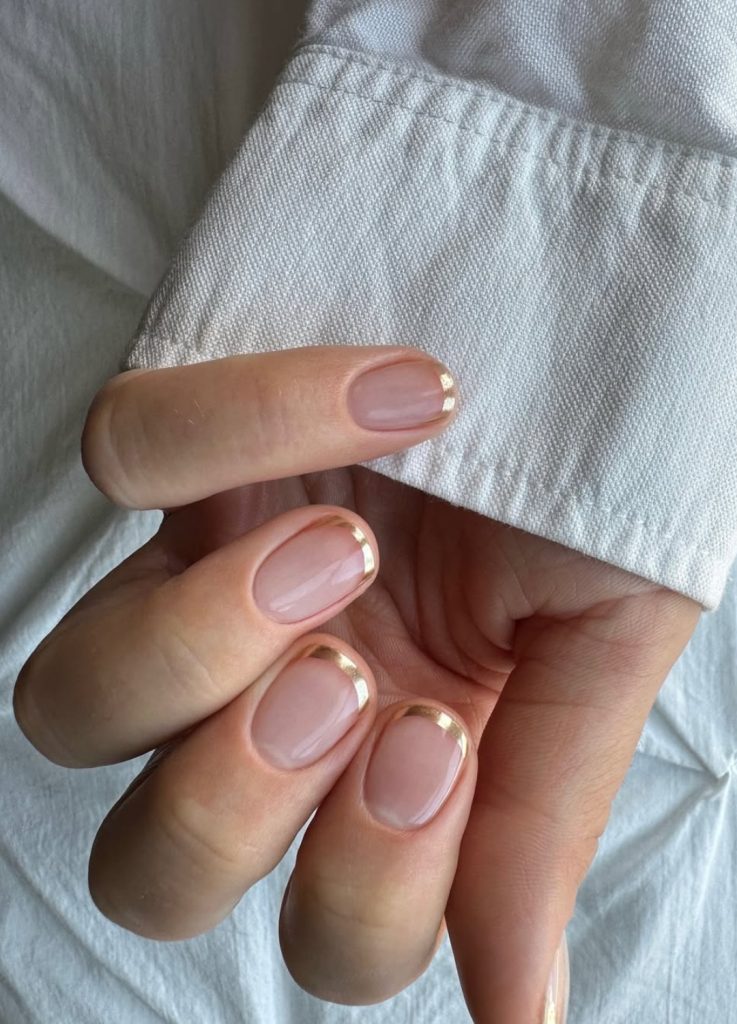 Milky white nails with a very thin, delicate gold micro-French tip.