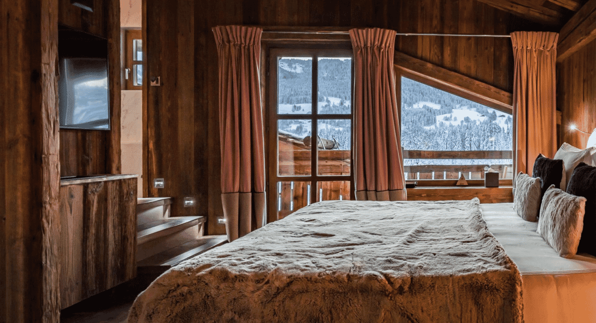 Cozy wooden bedroom with a large bed draped in a fluffy blanket and mountain views.