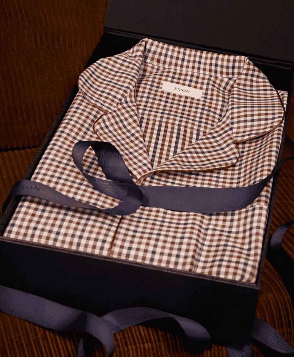 A folded Eton gingham-patterned pajama top inside a luxury black gift box.