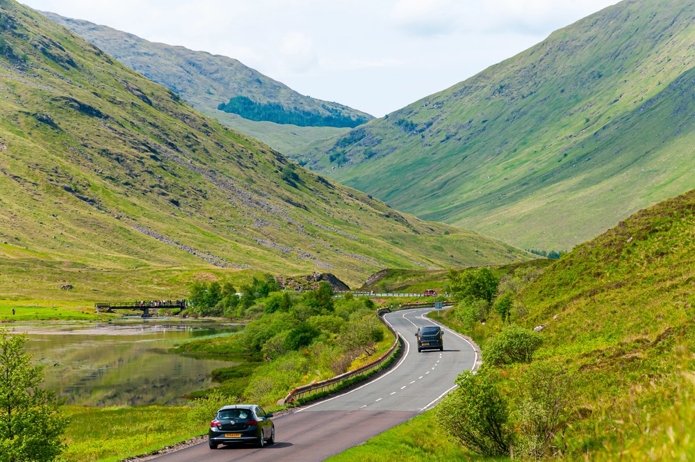 A winding mountain road cutting through vibrant green valleys and hills.